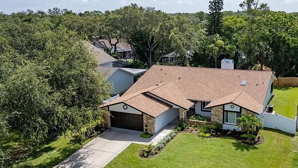 Aerial perspective of a house with a vast yard and numerous trees, highlighting the greenery and open space.