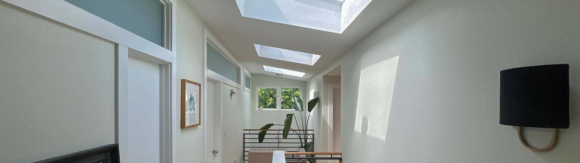 A hallway featuring skylights above and a door at the end, illuminated by natural light streaming through the skylights.