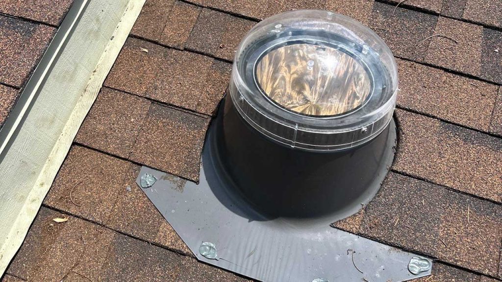 Roof exterior detail showing a fully installed VELUX TMR 010 Sun Tunnel acrylic dome and flashing kit sealed against asphalt shingles.